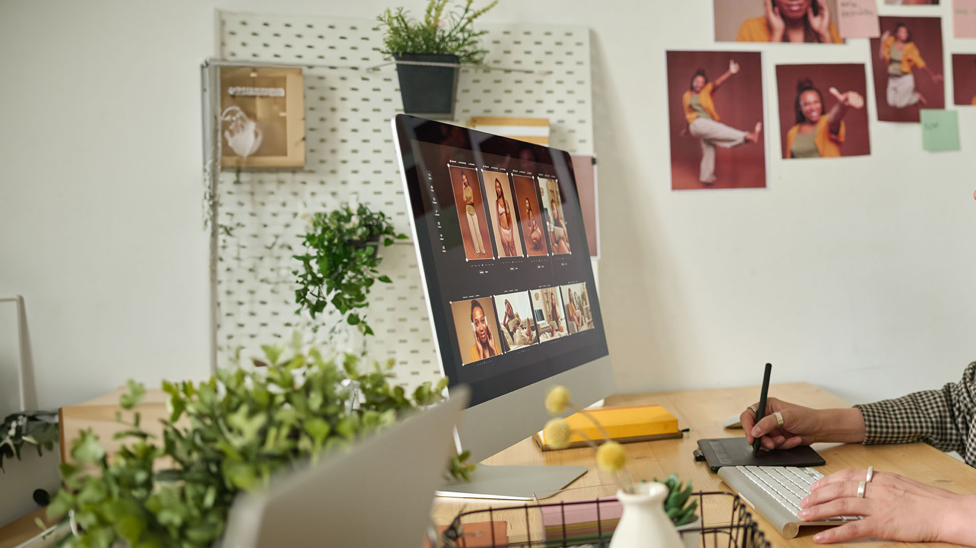 Grafik tabletle çalışan tasarımcı, ekranda kişisel portfolyo düzeni; duvarda basılı portre denemeleri