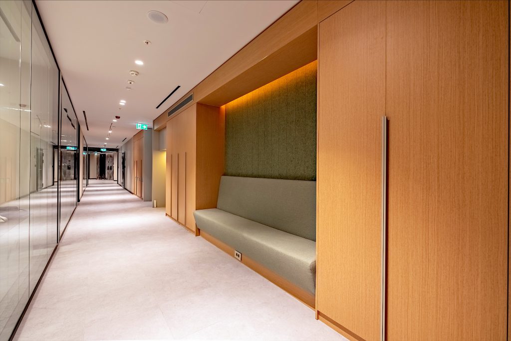 Cam bölmeli ofis koridoru ve ahşap nişli oturma alanı