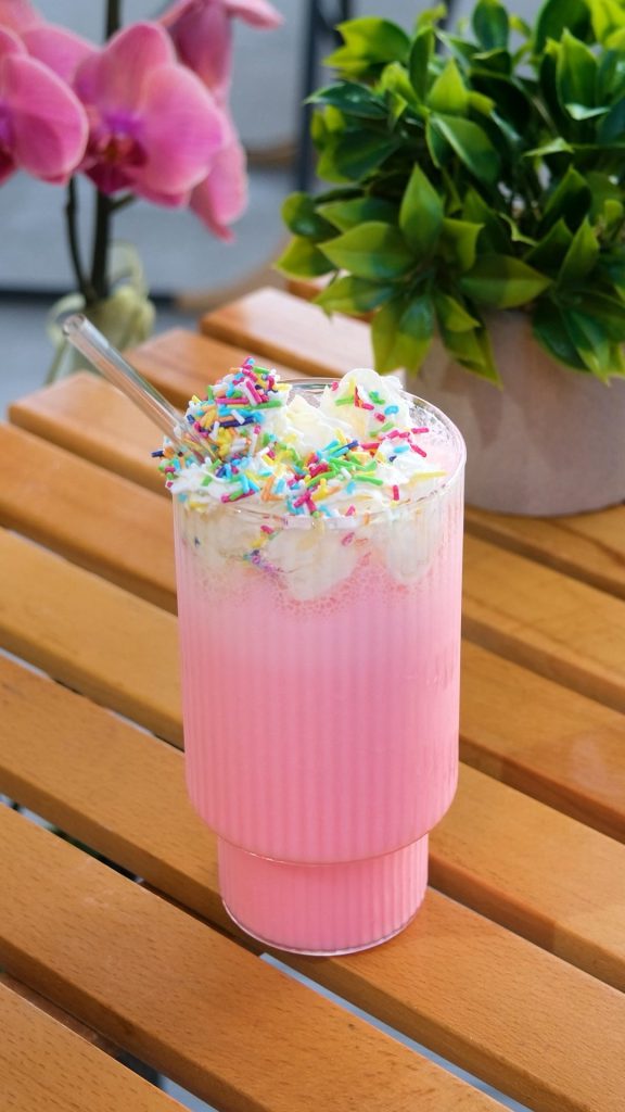 Ahşap masada renkli şekerlerle süslenmiş pembe çilekli milkshake